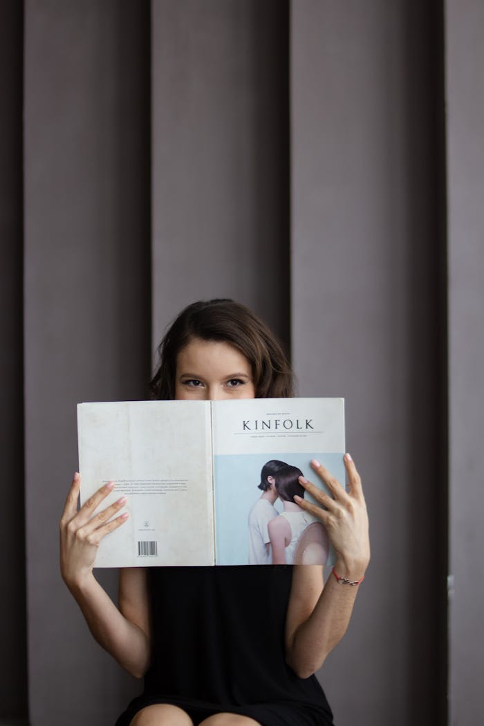 Services-01 Young woman reading Kinfolk magazine against a grey wall. Indoor setting, vertical shot.