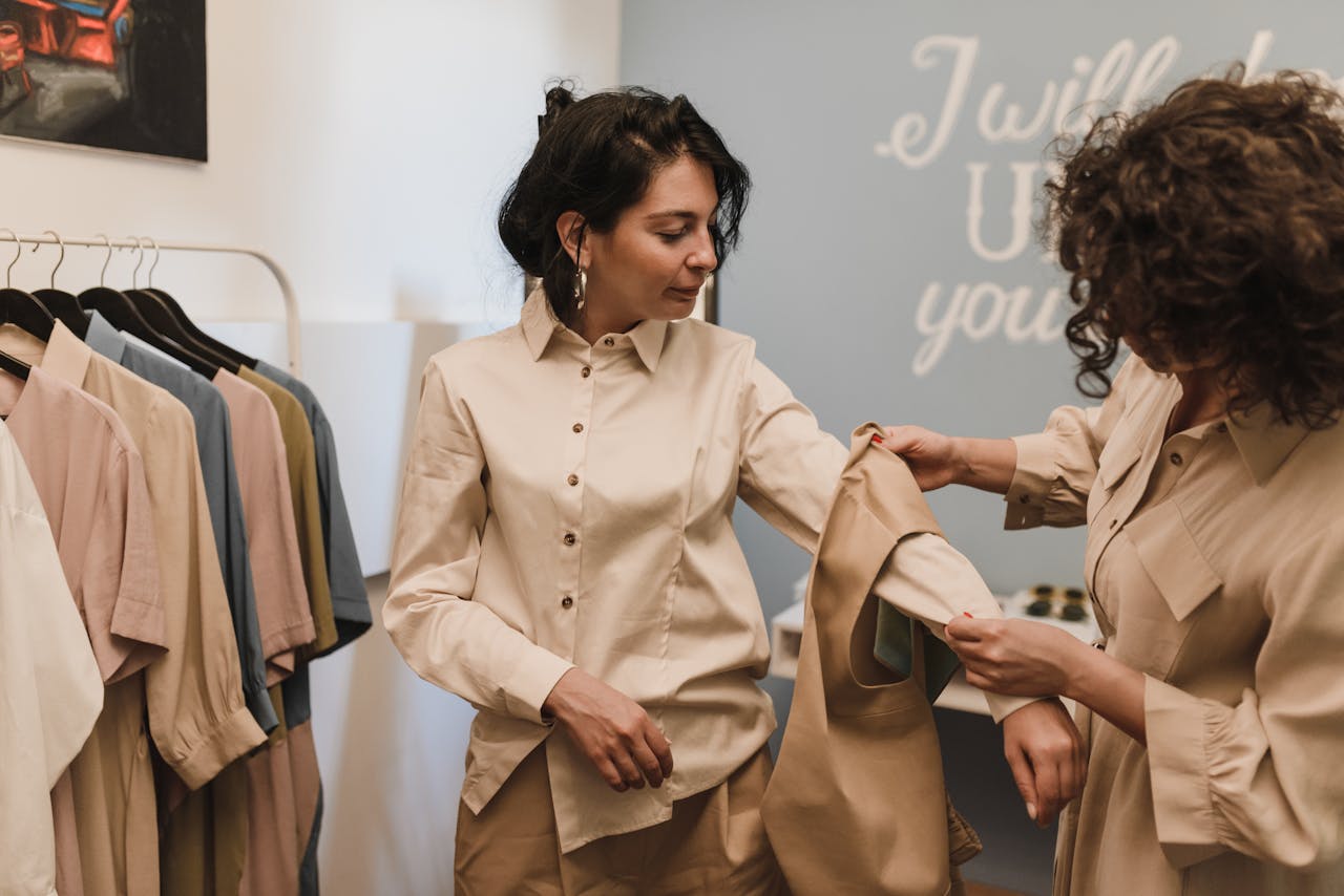 creative-03 Two women shopping in a boutique, examining a shirt together amidst a stylish clothing selection.